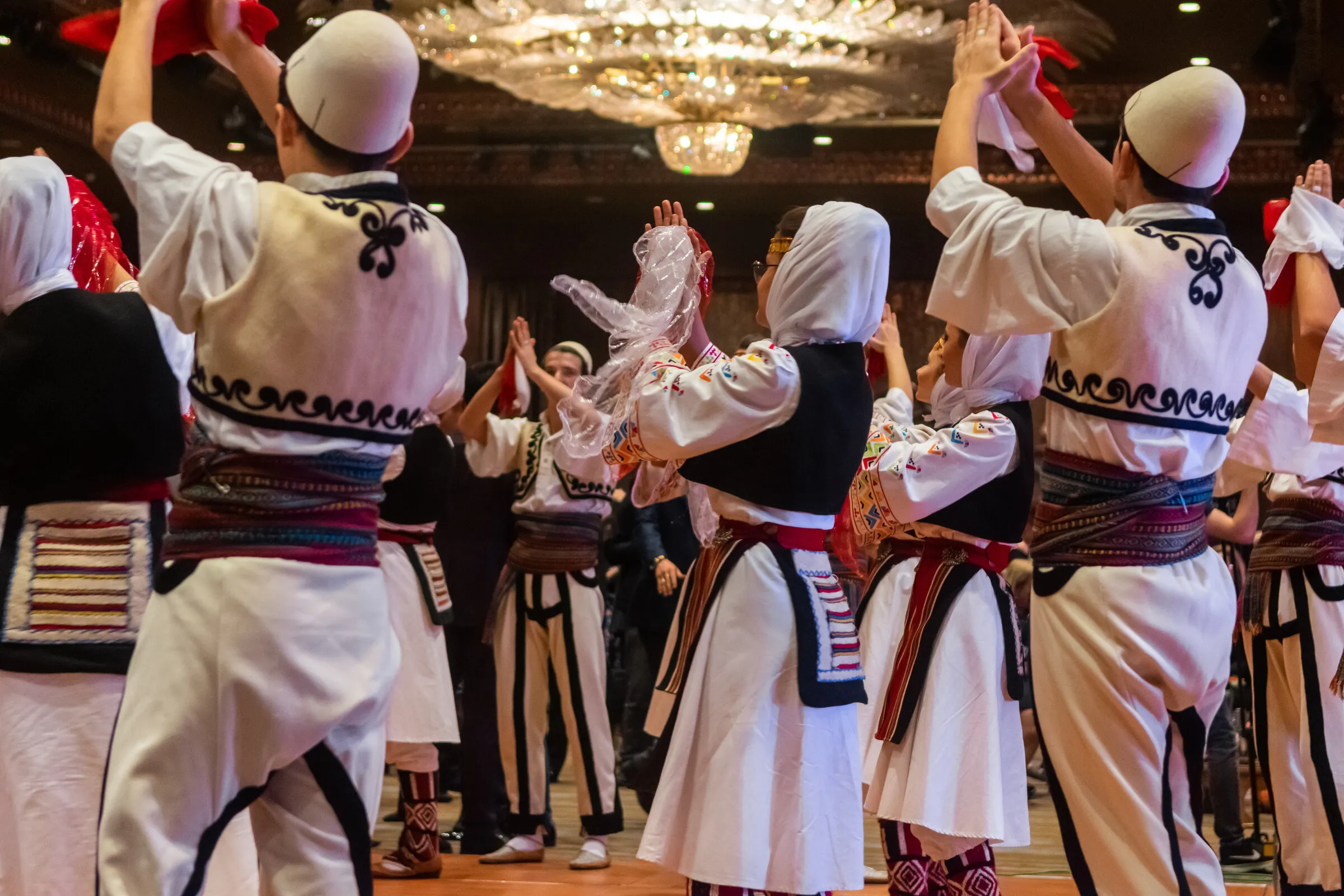 Dancers in traditional Albanian dress performing with raised hands at a community celebration